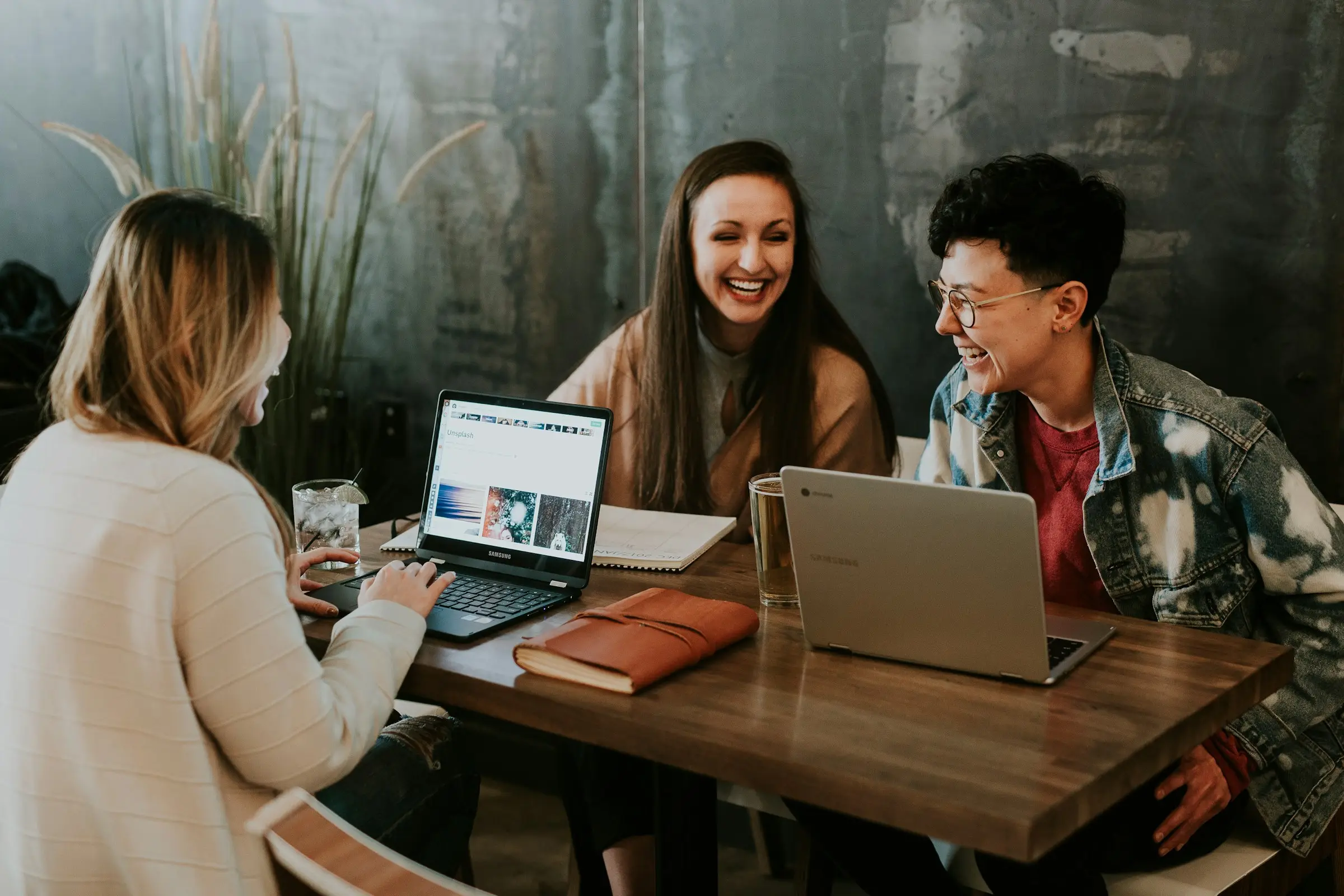 Students laughing over laptops at a shared table
