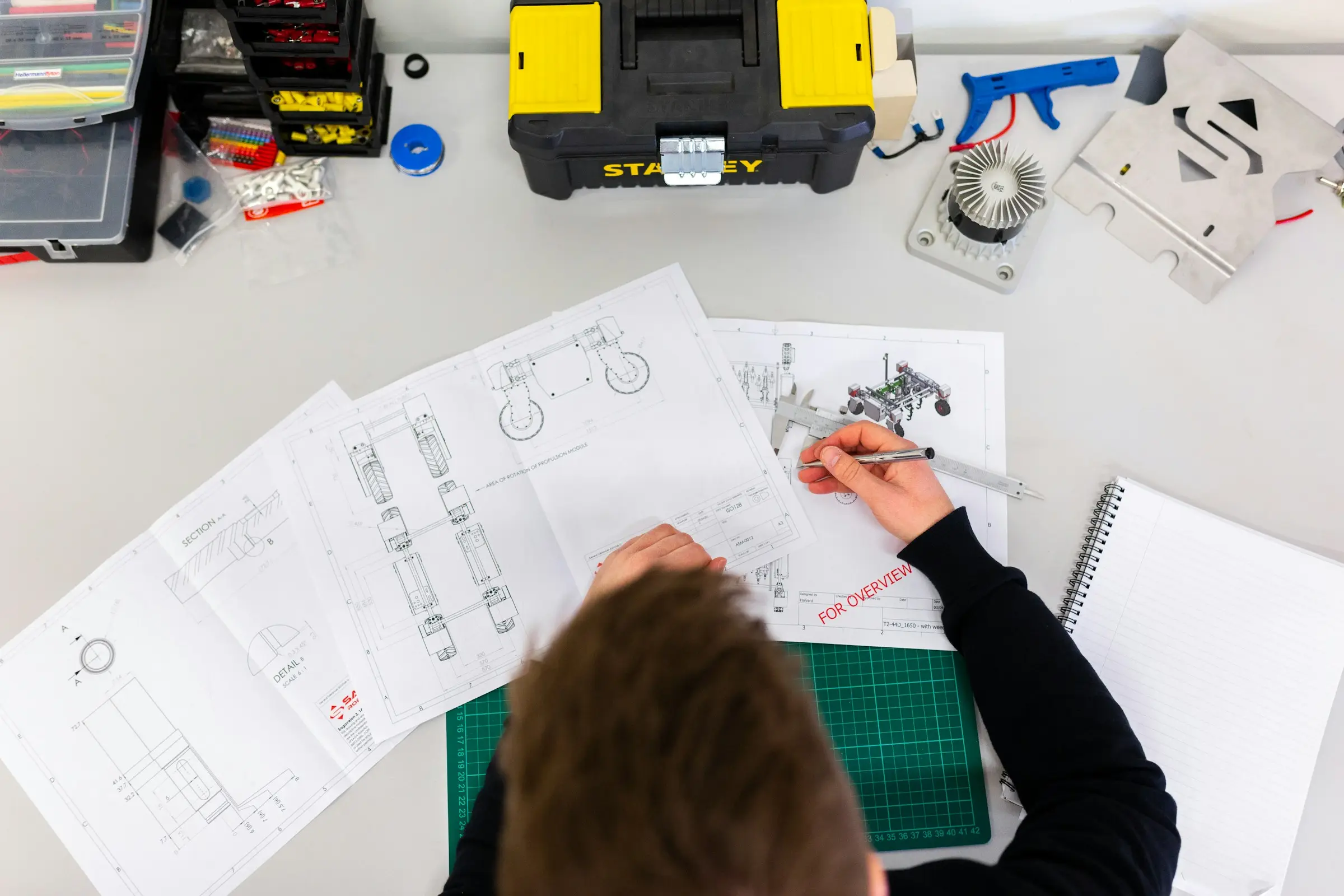 A maker sketching robot designs at a workbench, seen from above