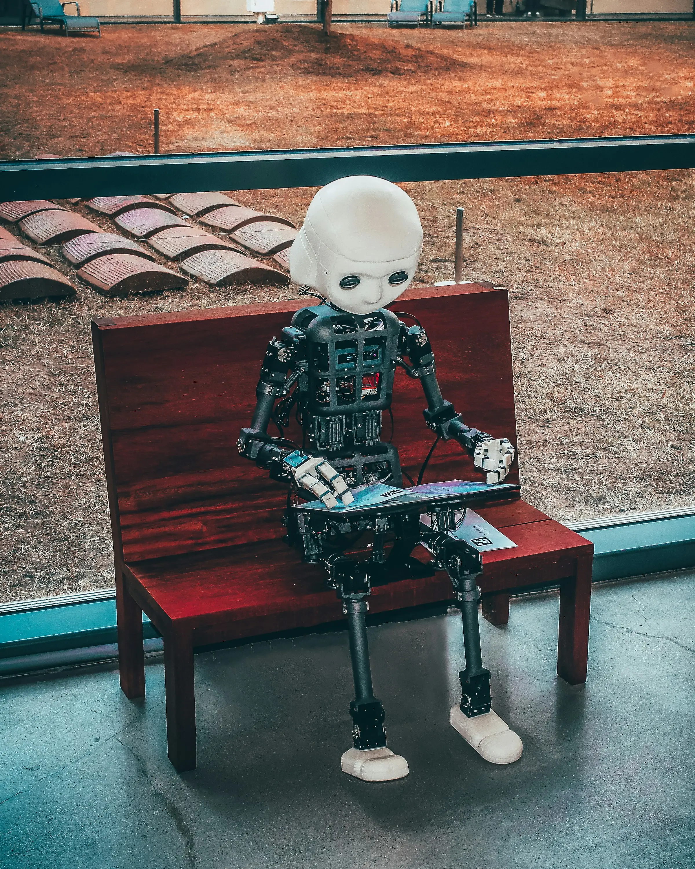 A small humanoid robot seated on a bench, reading